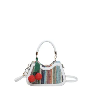 Vue détaillée du sac en paille tressée aux rayures colorées et pendentif cerise rouge.