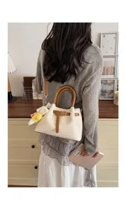Stylish cream bucket bag detail view featuring brown leather handles and cute plush charm.