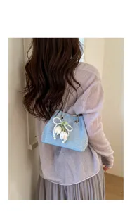 Close-up detail of light blue rhinestone chain bucket bag with pearl tulip decoration worn.