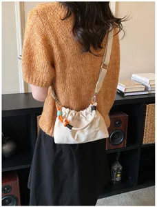 Vue détaillée du sac bandoulière élégant en toile blanche avec poignée tressée colorée.
