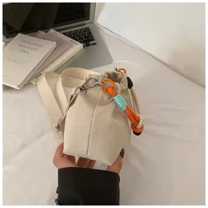 Sac bandoulière élégant en toile avec cordon tressé coloré et anneaux métalliques.