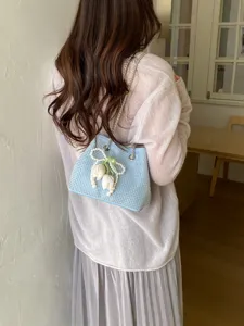 Detail shot of a stylish light blue rhinestone chain bucket bag with pearl tulip pendant.