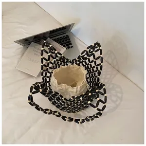 Close up detail of black and white beaded bucket bag with white inner pouch on white surface.