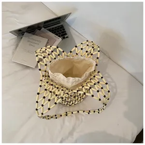 Detail shot of beige beaded woven bucket bag with canvas pouch on white surface with laptop prop.