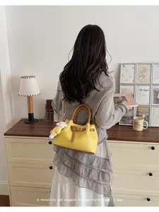Detail view of stylish yellow bucket bag with brown handles and charming plush pendant.