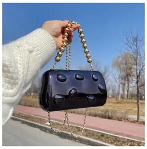 Primo piano borsa da sera in acrilico lucido, manico catena perle d'oro e texture bolle