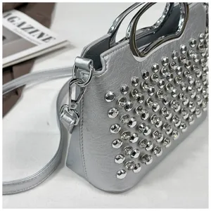 Détail de sac à main argenté clouté de strass avec poignées en métal et bandoulière.