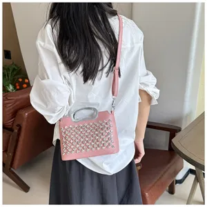 Détail de sac bandoulière rose en strass avec cristaux scintillants et poignée en métal.