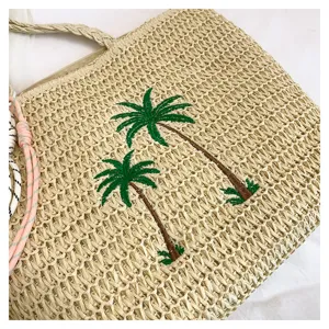 Details of the woven straw beach tote bag featuring elegant palm tree embroidery design.