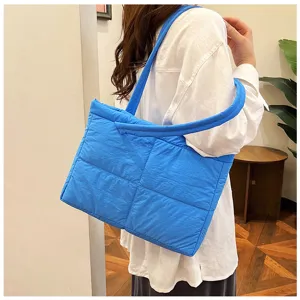 Close-up detail of a bright blue quilted puffer shoulder bag worn by a model indoors.