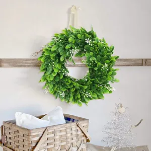 Artificial green leaf wreath detail showing lush foliage and white floral accents for wall decor.