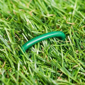 Detailaufnahme eines grünen U-förmigen Rasenankers im Kunstrasen für die Gartenbefestigung.