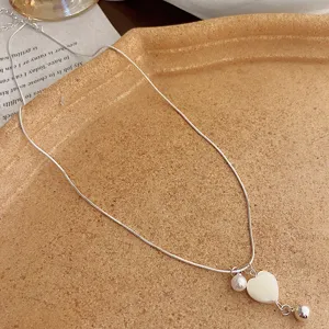 Close-up of elegant silver-tone clavicle chain featuring a heart shell pendant and pearl charm.