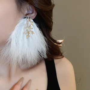 Gros plan de boucles d'oreilles pendantes en plumes blanches avec brindilles et perles.