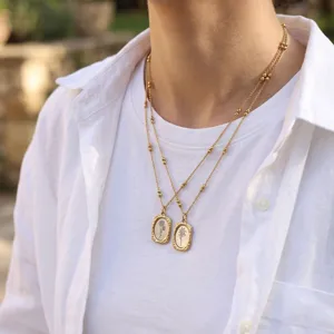 Close-up of double layered gold necklace with delicate floral engraved rectangular pendants.