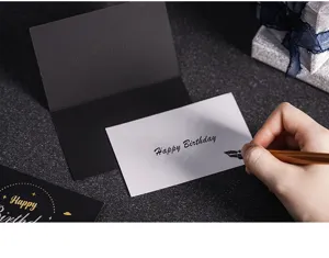 Vista detallada de tarjeta de felicitación con escritura a mano y sobre negro en escritorio oscuro.