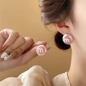Detailed close-up of pink round letter M ear studs worn by a model, elegant daily accessory.