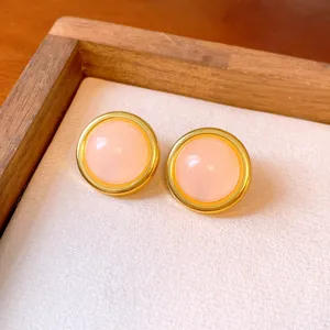 Pink round earrings featuring a polished gold-tone metal rim and smooth cabochon center detail.