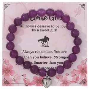 Bracciale di perle viola con ciondolo a cuore argentato su carta di presentazione rosa dettaglio