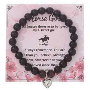Braccialetto di perle nere con ciondolo a cuore in argento su carta floreale rosa.