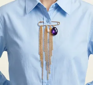 Primer plano de un broche dorado vintage de estrás morado con cadenas colgantes.