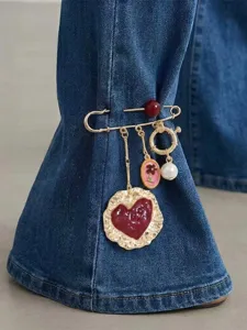 Close-up detail of retro safety pin brooch with red enamel heart, pearl, and charms on denim.