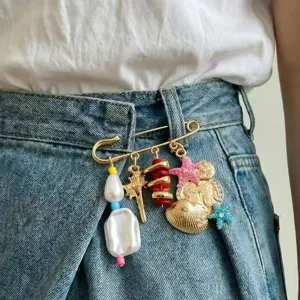 Vintage multi-charm safety pin brooch with pearls, seashells, and cute pendant details.