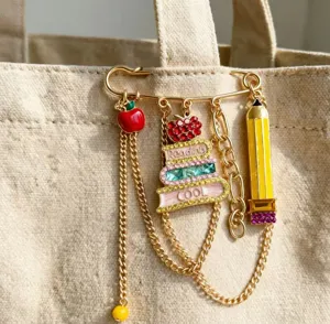 Campus style school book apple pencil metal chain brooch jewelry accessory detail closeup view.