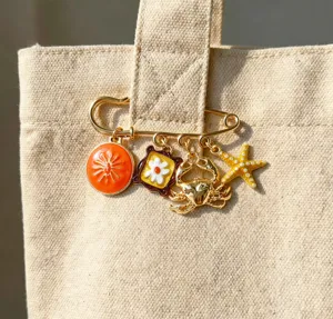 Gold tone alloy brooch featuring charming ocean elements like sun, flower, crab, and starfish.