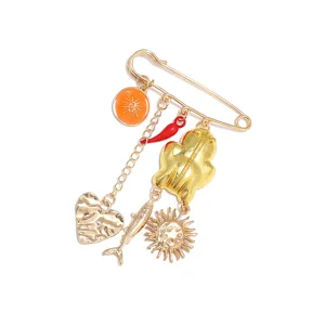 Detailed shot of gold safety pin brooch featuring cute orange, chili, heart, and fish charms.