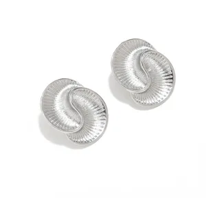 Dettaglio in primo piano di orecchini testurizzati a spirale geometrica argentata.