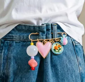 Nahaufnahme einer bunten Brosche mit Herz, Blumenanhänger und Perlen am Jeansbund.