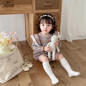 Detailed shot of cute baby floral long sleeve romper in warm cozy wooden interior scene.