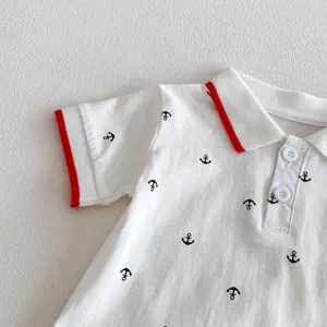 Close-up of infant baby boy short sleeve polo romper with anchor print and red trim details.