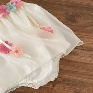 Dettaglio della tutina estiva per neonati con fiori, tessuto scintillante e decorazioni.