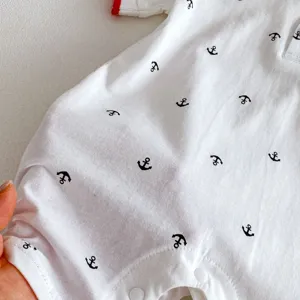 Close-up detail of white baby romper featuring black anchor print and red collar trim.