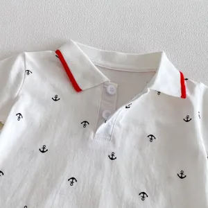 Detail shot of white baby romper collar with black anchor prints and red trim design.