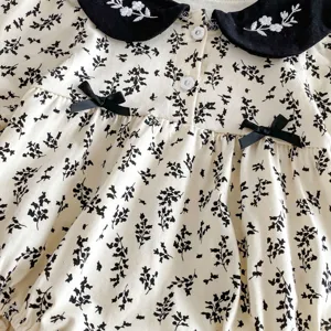 Lindo body de bebé con estampado floral, cuello bordado negro y bonitos lazos para el otoño.