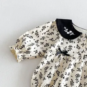 Detalle de pelele para bebé con estampado floral, cuello contraste negro y elegante bordado.