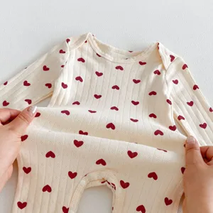 Close-up of baby long sleeve cotton romper, beige ribbed fabric with red heart print.