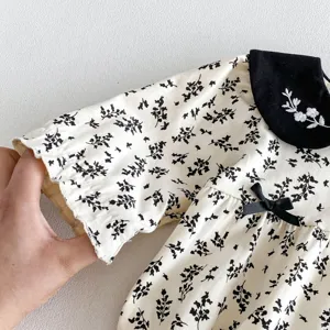 Detalle de mameluco de bebé con estampado floral, cuello negro, bordado blanco y un lazo.