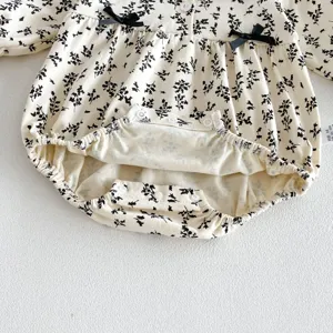 Detalle de pelele para bebé con estampado floral, lazos negros y botones de presión útiles.