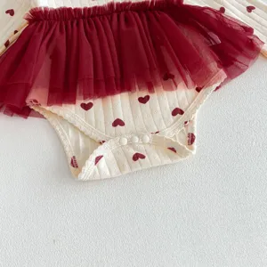 Detailopname van de babyromper met rode tulen rok, hartjesprint en handige drukknoppen.