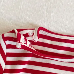 Primer plano del cuello del body de bebé a rayas rojas y blancas, tejido suave, botones prácticos.