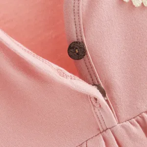 Detalle de mameluco rosa de algodón para bebé niña, con botones de madera y delicado cuello de encaje.