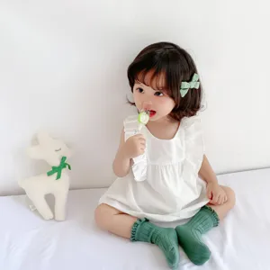 Dettaglio outfit estivo bambina, abito bianco con volants, calzini verdi e molletta.