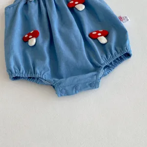 Adorable mameluco de mezclilla azul para bebé con apliques de hongos rojos y botones a presión.