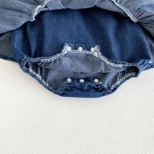 Dettaglio ravvicinato della tutina in denim per neonata con pratici bottoni a pressione.