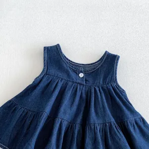 Dettaglio ravvicinato del vestito in denim per bambina con balze plissettate e bottone.