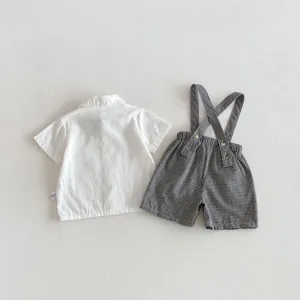 Detailed view of baby boy summer short sleeve white shirt and black checkered suspender shorts.
